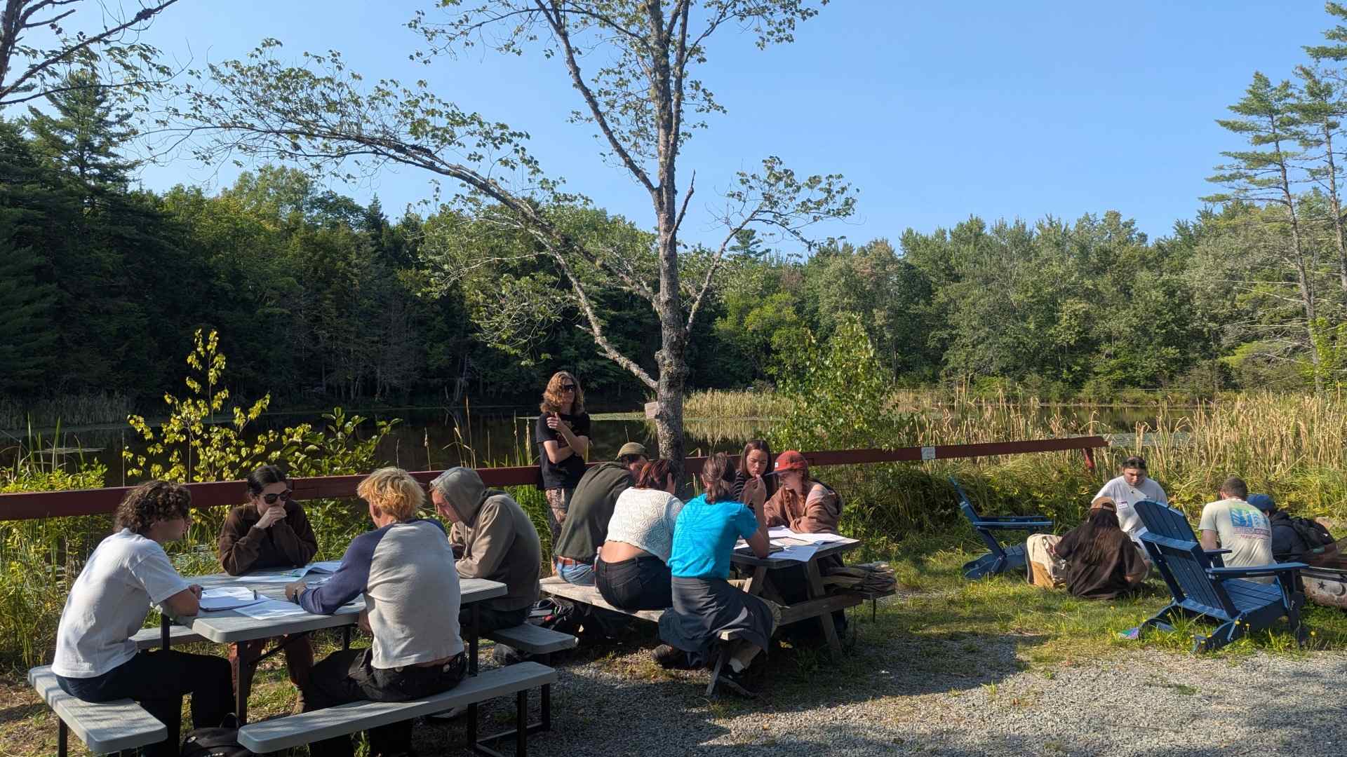 Students listening to lecture outside at picnic tables.